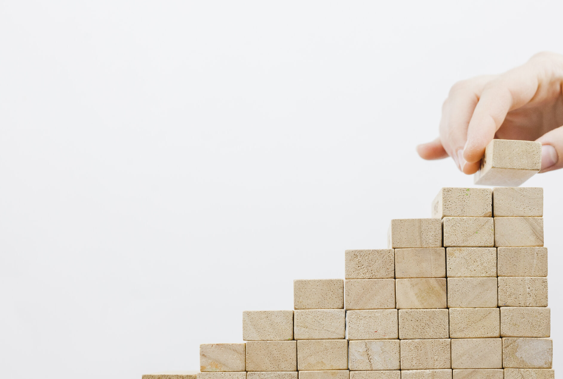 steps constructed of wooden blocks with a hand adding more blocks to the top. Meant to represent building a solid foundation of knowledge management.